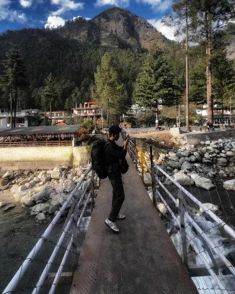Ansith on a footbridge over a mountain river, taking a photo