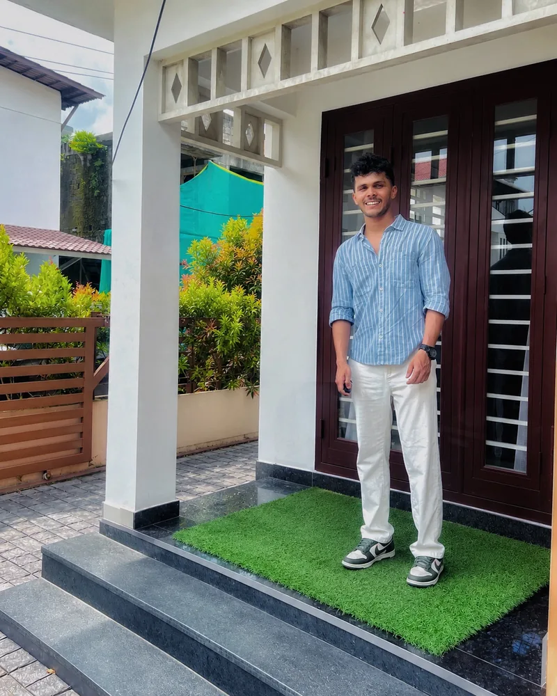 Ansith smiling in a striped blue shirt and white trousers at a doorway