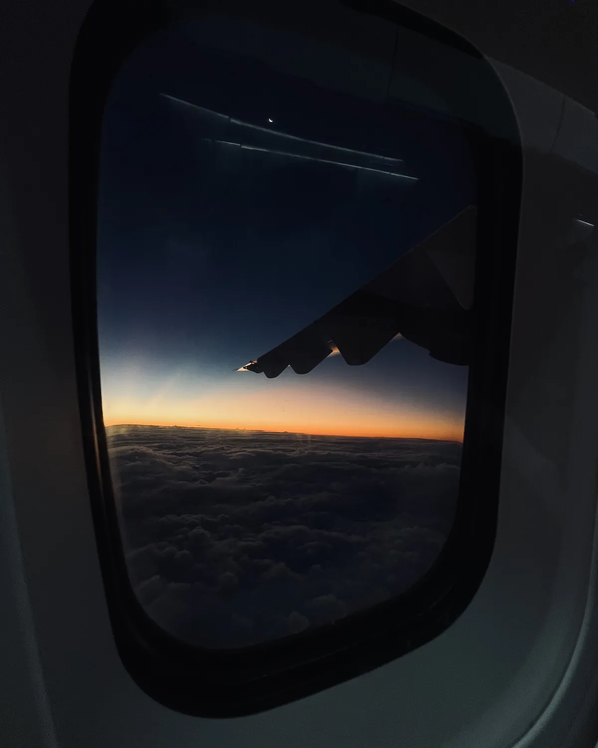 An aeroplane window showing a wing above clouds at sunset