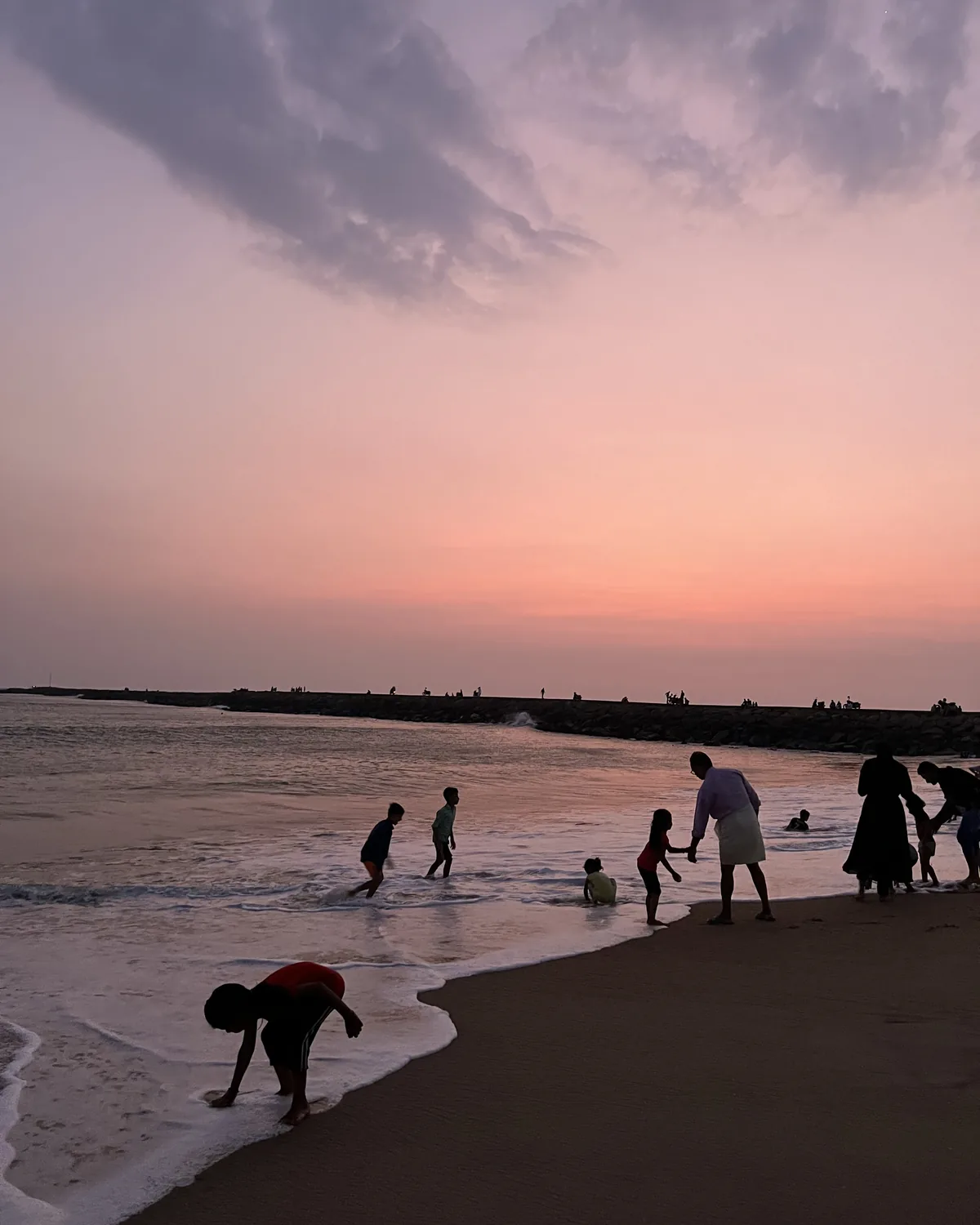 Children and families playing in the surf at a pink and lilac sunset